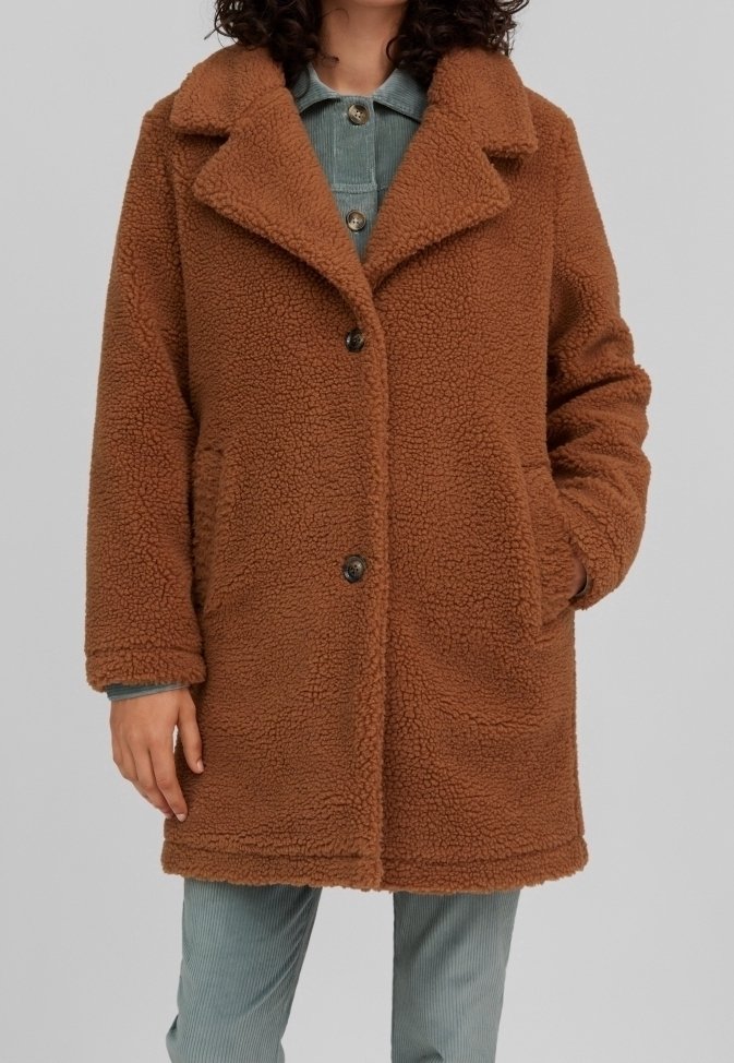 Manteau marron texturé mi-long avec deux boutons et poches latérales porté sur une chemise bleue à boutons et un pantalon.