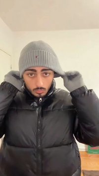 Szürke bordázott sapka logóval, fekete pehelykabát és szürke kesztyűk. A sapka szorosan illeszkedik, a kabát magas gallérral és cipzárral rendelkezik.