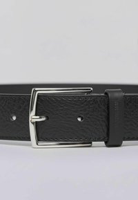 Czarny skórzany pasek o teksturowanej powierzchni, ze srebrną prostokątną klamrą i wieloma otworami do regulacji. Zawiera małą czarną etykietę jako akcent.