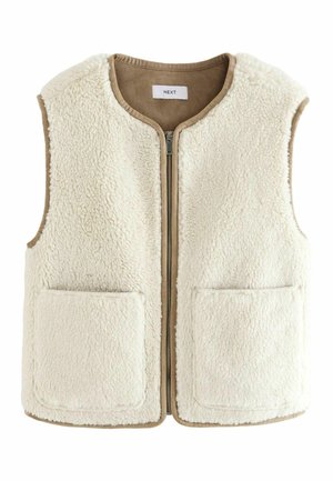 Personne portant un gilet sans manches crème et duveteux et un jean sombre taille haute, vue de dos sur un fond uni.