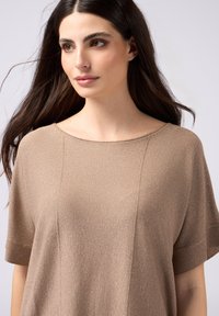 Top in maglia beige con una texture morbida, scollatura ampia a barca, maniche corte e una leggera lucentezza. Presenta dettagli a costine sulle maniche.