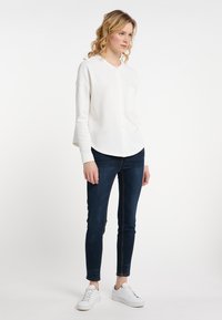 Bílá košile s knoflíky a zaobleným lemem, doplněná tmavými skinny džínami a bílými teniskami. Jednoduchý, ležérní outfit.