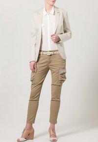 Béžový blazer přes bílou blůzu, ve spojení s khaki cargo kalhotami se bočními kapsami a světle béžovými wedge botami s kotníkovými šněrováním.