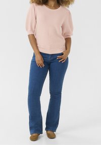 Jasnoróżowy sweter z prążkowanym wzorem i krótkimi bufkami, połączony z dopasowanymi niebieskimi dżinsami i brązowymi zamszowymi butami. Sweter ma okrągły dekolt.