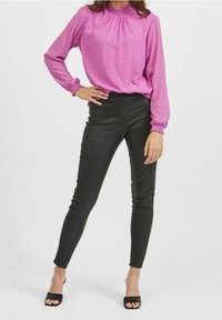 Rosa långärmad blus med en texturerad chevronmönster och rynkad halsringning, kombinerad med svarta figurnära läderbyxor och öppen tå klackar.