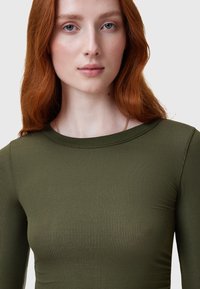 Maglietta a maniche lunghe a costine in verde oliva. Presenta un collo rotondo e una superficie liscia con una leggera lucentezza.