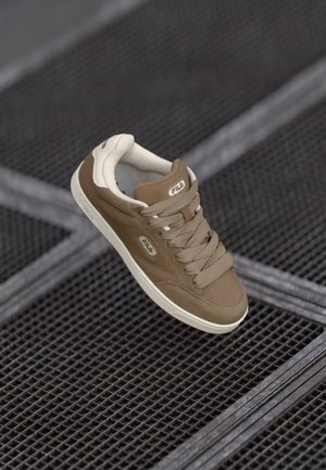 Brune lærersneaker med beige detaljer, rund tå, polstret krage og snørebånddesign. Har logo detalj på siden og teksturert såle.