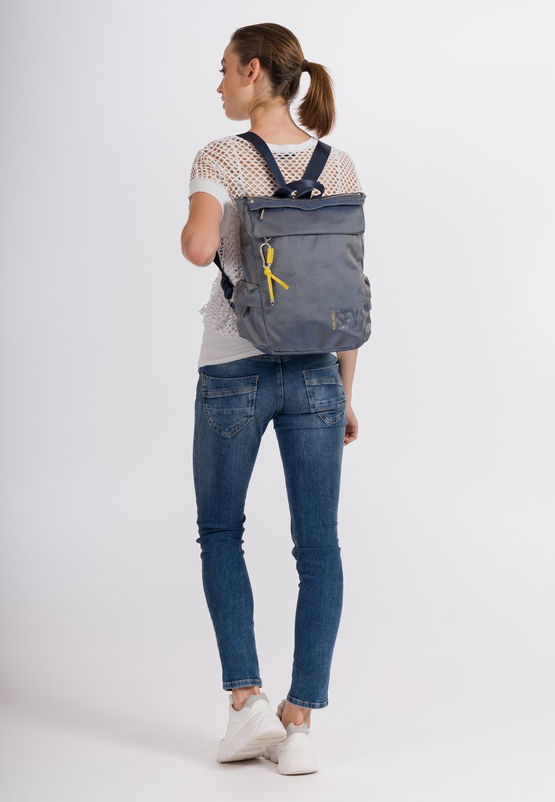 Mochila gris con diseño de tapa enrollable, que presenta un acento amarillo, correas ajustables y una forma estructurada, mostrada en una persona.