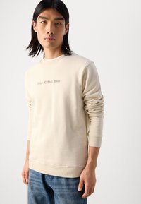 Kreminės spalvos džemperis, pagamintas iš minkštos medvilnės, su nusmukusiais rankogaliais ir apvaliomis kaklo iškirpėmis. Subtiliai šviesiai ruda "Marc O'Polo DENIM" logotipas.