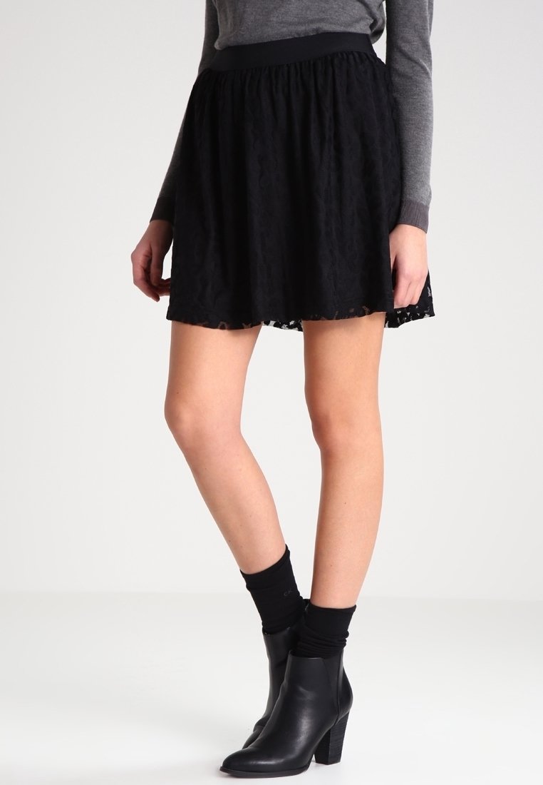 Jupe en dentelle noire avec un design évasé, taille élastique et ourlet festonné. Portée avec des bottines noires et des chaussettes montantes.