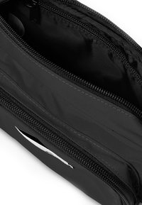 Sort nylon taske med flere åbninger, der har glatte lynlåse og en tekstureret overflade. Indvendigt er den foret med et blødt stof.