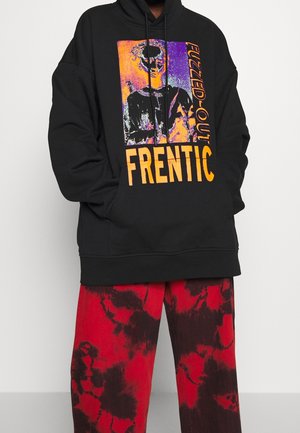 Czarna bluza z kapturem z pomarańczowo-fioletową grafiką popiersia i napisem „FUZZED-OUT FRENTIC”, zestawiona z czerwono-czarnymi spodnimi tie-dye.