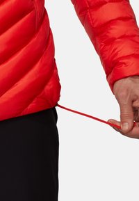 Giacca isolante rossa con design trapuntato, dotata di cordino all'orlo. Il materiale esterno appare liscio e lucido, con una vestibilità aderente.