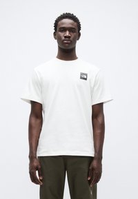 Λευκό βαμβακερό t-shirt με κοντά μανίκια και στρογγυλή λαιμόκοψη, με μαύρο τετράγωνο λογότυπο στο αριστερό στήθος. Απλός και λιτός σχεδιασμός.