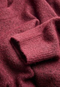 Bordo megztinis, pagamintas iš audinio su tekstūruota paviršiumi, minkštu ir pūkuotu jausmu bei raukšlėmis rankogaliais.