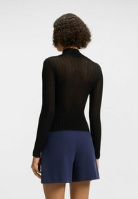 Haut noir à manches longues côtelé avec un col haut et une coupe slim, fabriqué en tissu texturé léger, accompagné de shorts bleu marine.