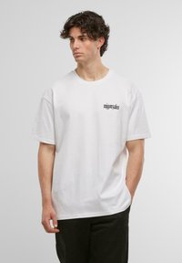 White cotton t-shirt featuring a black logo on the left chest. Relaxed fit with short sleeves and a classic crew neckline.