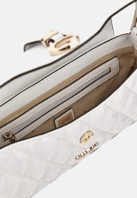 Bílá prošívaná kabelka se zlatými kovovými prvky, která má strukturovaný design, vnitřní kapsy a hladký, texturovaný povrch.