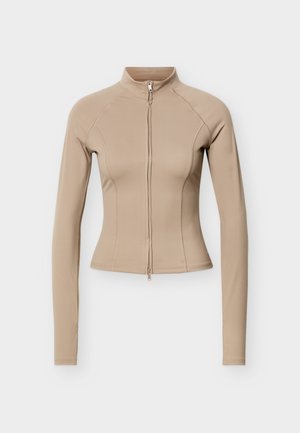 Kreminės spalvos trumpas švarkelis ilgomis rankovėmis, su aukštu apykakliu ir priekyje užtrauktuku, prigludęs modelis su matomomis siūlių detalėmis.