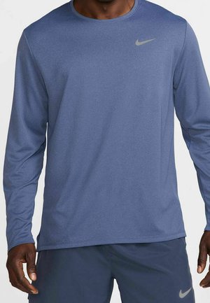 Homme portant un t-shirt de sport Nike bleu à manches longues et un short assorti avec les logos Nike sur la poitrine et la cuisse gauche.