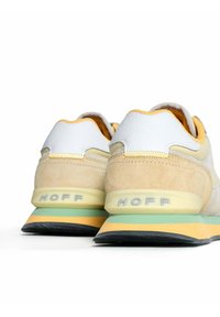 Zapatillas deportivas con una mezcla de cuero blanco, ante beige y acentos amarillos. Suela de goma con detalles en verde y naranja. Logo en relieve en el talón.
