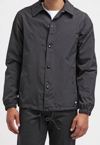 Svart lättviktsjacka med krage, tryckknappar, elastiska ärmslut och sidofickor. Tillverkad av glatt, matt tyg.