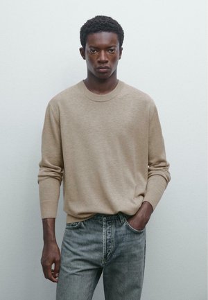 Beige knit sweater with a crew neckline and ribbed cuffs, paired with light gray jeans. The texture appears soft and smooth.