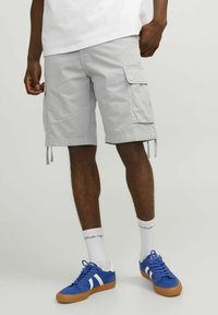 Shorts cargo gris clair avec poches latérales, liens ajustables et coupe loose, accompagnés de baskets bleues et de chaussettes blanches avec texte.