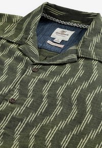 Chemise à manches courtes, verte et blanche avec un motif, dotée d'une fermeture à boutons, d'un col et d'un tissu texturé à rayures diagonales. La doublure intérieure est bleue.