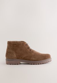Bottine marron en daim avec laçage à l'avant et semelle en caoutchouc dotée de crampons profonds pour une utilisation en extérieur, montrée de profil sur un fond neutre.