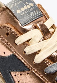 Sneaker in pelle di rame metallico con lacci avorio, dotata di un accento in suede nero e un'etichetta logo blu sulla linguetta.
