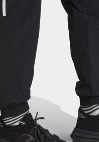 Svarta joggingbyxor med elastiska muddar, i en snygg design, kombinerade med svarta skor och randiga svarta och vita strumpor. Mjuk tygstruktur.