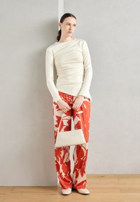 Off-white long-sleeve top with gathered detailing; red floral wide-leg pants; matching small light bag; cream pointed-toe shoes.
