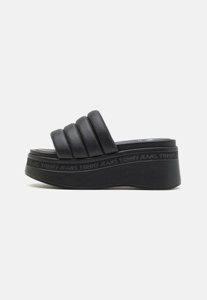 Black platform slide sandals with three wide, pleated straps and a textured sole. Features embossed "TOMMY JEANS" branding around the base.
