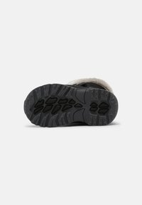Schwarze Schuhsohle mit strukturiertem Grip-Muster, ausgestattet mit tiefen Profilrillen und einem weichen, flauschigen Futter im Knöchelbereich für zusätzlichen Komfort.
