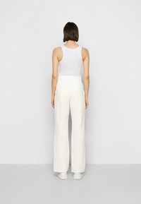 Calças largas brancas com cintura alta, apresentando bolsos traseiros e uma textura de tecido suave, combinadas com uma camisola branca justa.