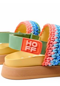 Sandalias de plataforma coloridas con correas sintéticas verdes, parte superior de textil trenzado en rosa, azul y verde, con una etiqueta de logo naranja y suela acolchada.
