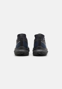 Zapatillas deportivas en negro y azul marino con un acabado texturizado, que cuentan con un cuello acolchado, una lengüeta de tirón y una suela de goma con patrón de relieve.