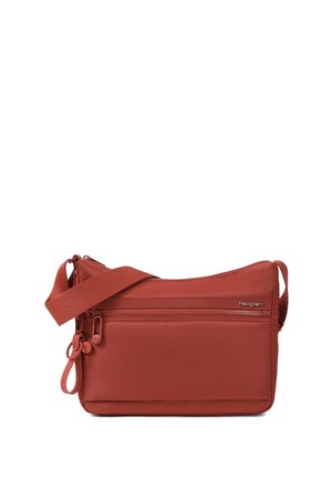 Kompaktná crossbody taška farby hrdze s nastaviteľným remienkom, dvoma prednými vreckami na zips a malým logom Hedgren v pravom hornom rohu.