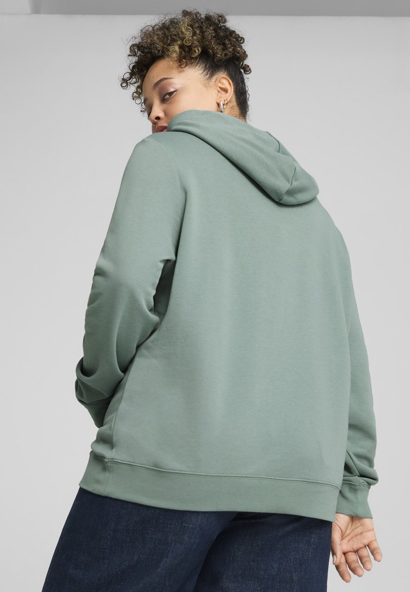 Felpa con cappuccio in morbido tessuto verde, caratterizzata da un taglio rilassato, polsini e vita a coste, con una texture liscia e un design minimale.