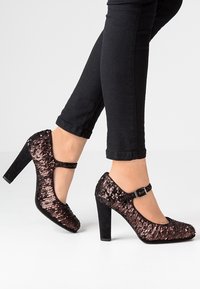 Chaussures à talons hauts noires avec un dessus en sequins, bout rond, bride de cheville avec boucle et un épais talon carré.
