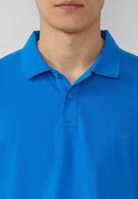 Blaues Baumwoll-Polohemd mit Kragen, zwei Knöpfen und gesticktem Logo auf der linken Seite. Strukturiertes Gewebe mit glatter Oberfläche.