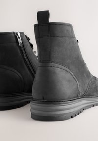 Schwarze Wildleder-Stiefeletten mit strukturierter Oberfläche, seitlichem Reißverschluss und mehrschichtiger Gummisohle. Verfügen über eine Schlaufe an der Ferse zum einfachen Anziehen.