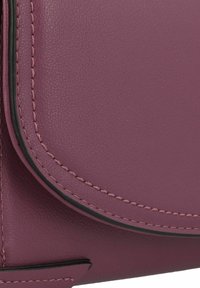 Esquina de bolsa de cuero morado, con textura suave, costuras de borde negro en contraste y un diseño elegante. Sin herrajes ni acentos visibles.