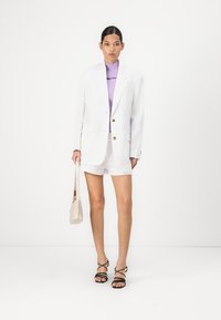 White oversized blazer with gold buttons, purple ribbed top, white shorts, black strappy heels, and a beige handbag. Smooth textures throughout.
