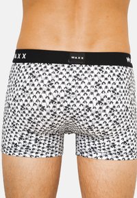 Boxer-briefs noir et blanc avec un motif de pingouins répétitif, en tissu doux, et une taille noire avec le logo "WAXX".