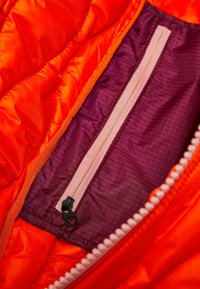 Oranje geïsoleerde jas met een binnenvoering die een paarse ritszak heeft, met een roze rits en een geruite textuur.