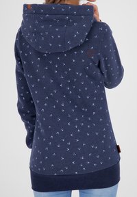Sudadera navy con un sutil patrón de pequeños puntos azules, presenta una capucha con cordón y un dobladillo texturizado, fabricada con una tela suave.