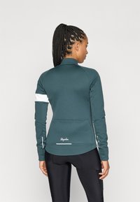 Chaqueta de ciclismo teal con mangas largas, cuello alto, detalles blancos y logotipo de Rapha. Material suave y elástico diseñado para la comodidad y el rendimiento.