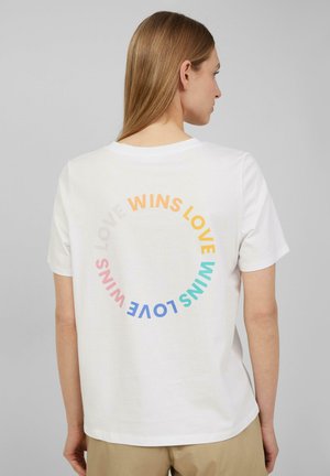 T-shirt en coton blanc à col rond, avec un graphique circulaire en texte multicolore au dos qui dit "L'AMOUR GAGNE." Manches courtes.